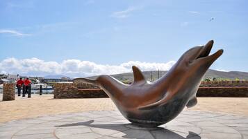 A large bronze sculpture of a hand in a public space with a clear sky and distant mountains.