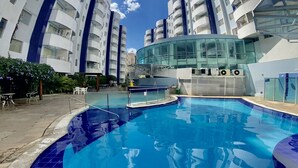 A modern hotel with a swimming pool, multiple balconies, and a glass facade.