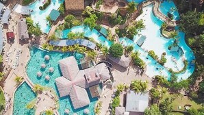 Luftaufnahme eines Resorts mit mehreren Schwimmbecken, Liegebereichen und tropischer Bepflanzung.