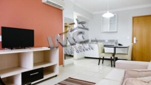 A living room with a TV, a sofa, a dining table, and a kitchen area.