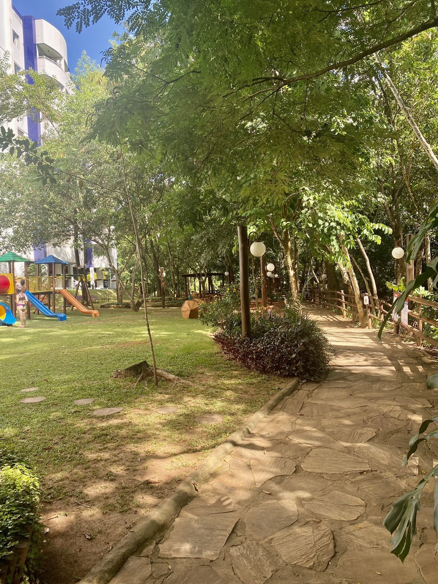 Um parque com um parquinho, uma trilha pavimentada e um edifício ao fundo.