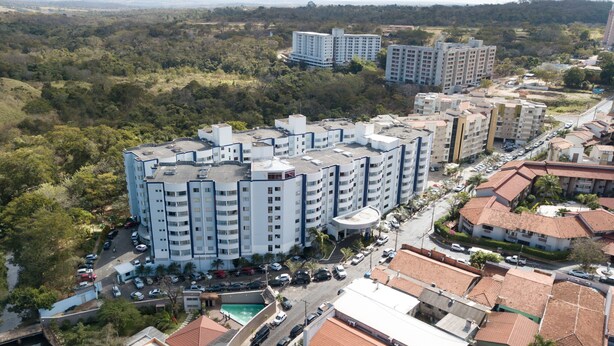 A high-rise residential building with multiple balconies, surrounded by greenery and other residential structures.