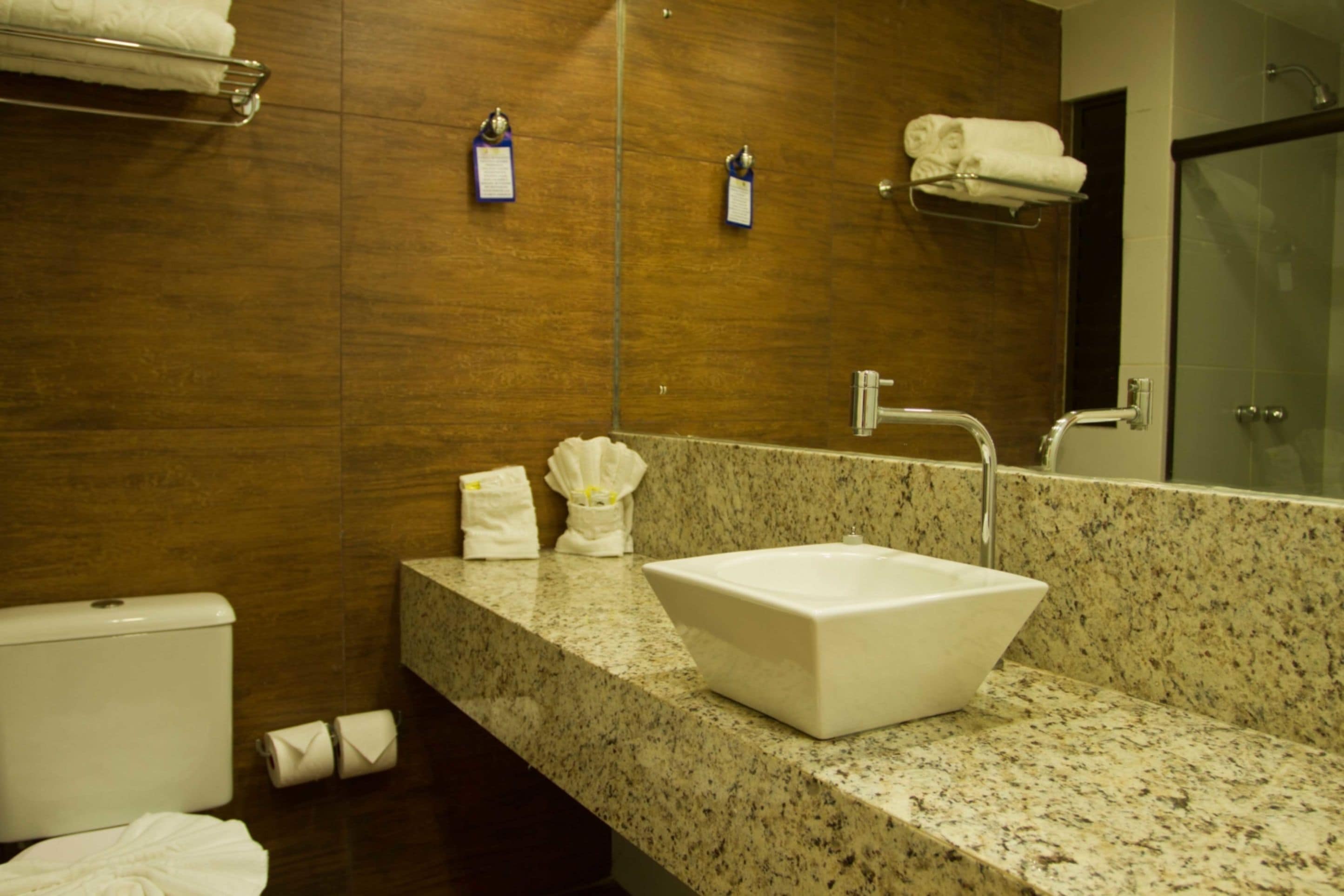 Un bagno con lavandino bianco, piano di lavoro in marmo, parete in legno e cabina doccia in vetro.