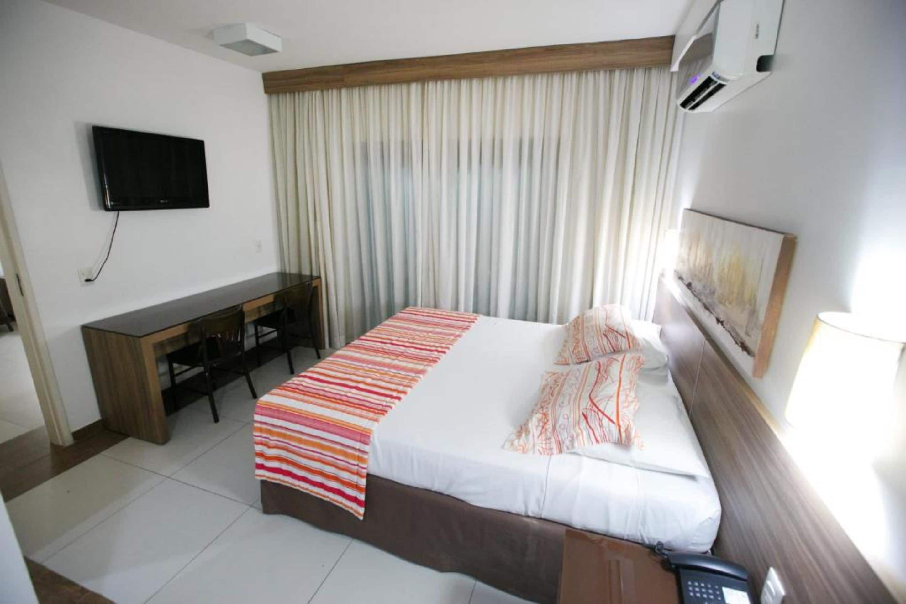 Une chambre d’hôtel équipée d’un lit, d’un bureau, d’une chaise, d’une télévision et d’une fenêtre avec des rideaux.