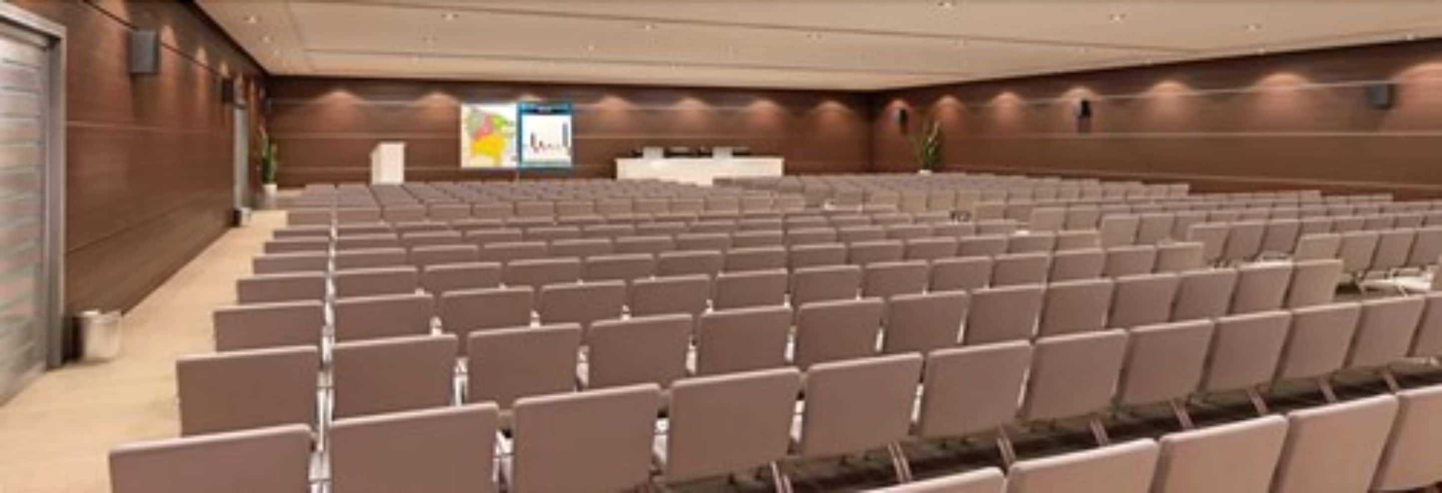 A conference room with rows of chairs, a podium, and a large poster on the wall.