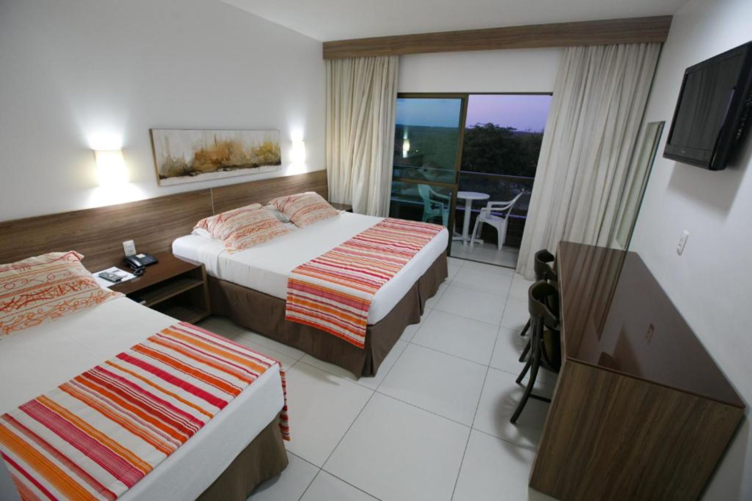 Habitación de hotel con dos camas, un escritorio, una silla, un televisor y un balcón con vistas.