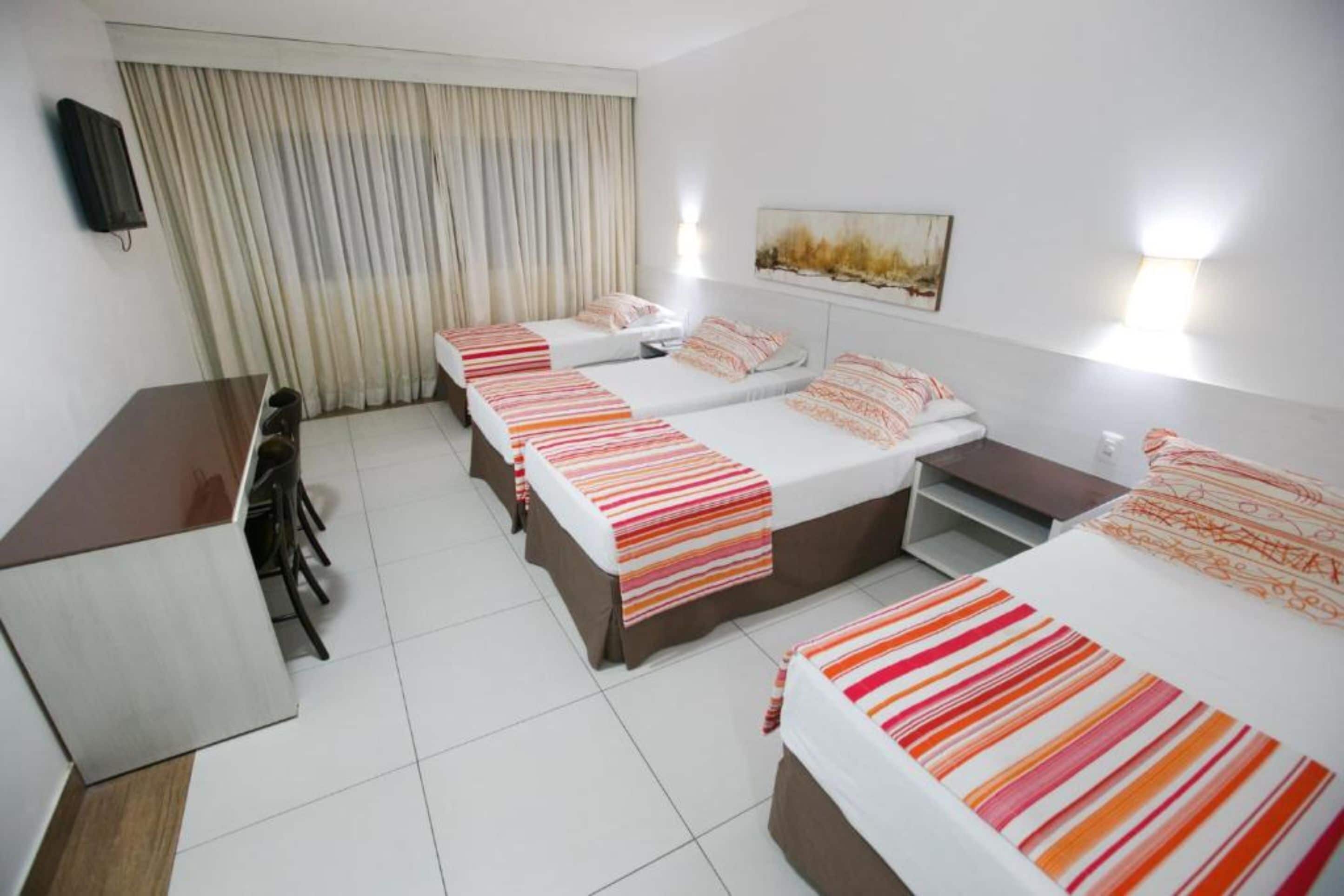 A hotel room with three beds, a desk, and a chair.