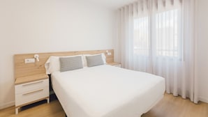 Habitación de hotel ordenada con cama de madera, ropa de cama blanca y mesita de noche con lámpara.