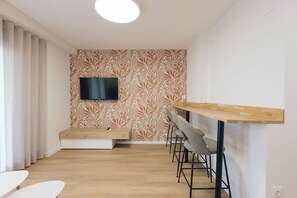 A modern room with a flat-screen TV mounted on a patterned wall, a wooden bench, and a bar area with stools. - Pio XII Apartments (Valencia)
