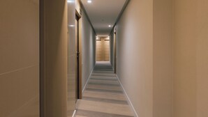 Un largo y estrecho pasillo de hotel con alfombra a rayas, puertas de madera y un letrero con número sobre cada puerta.