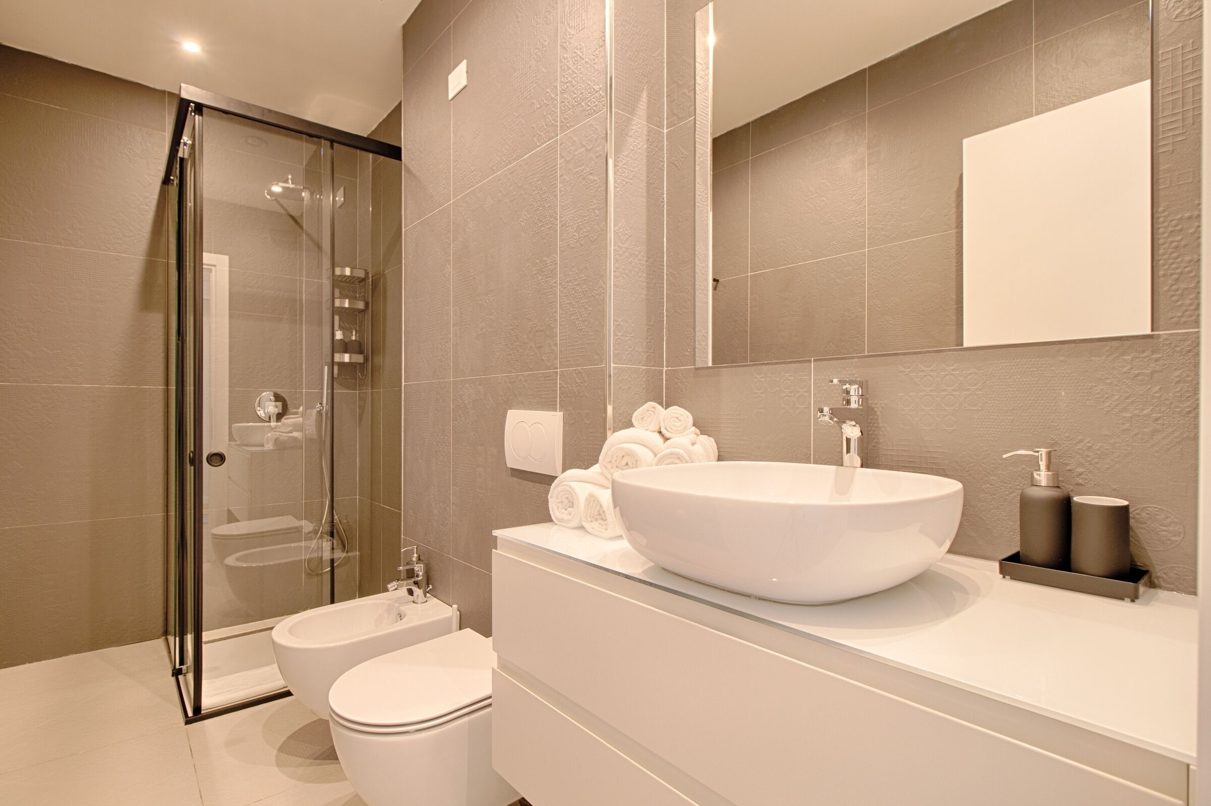 Un baño moderno con cabina de ducha de vidrio, un lavabo blanco y un espejo grande.