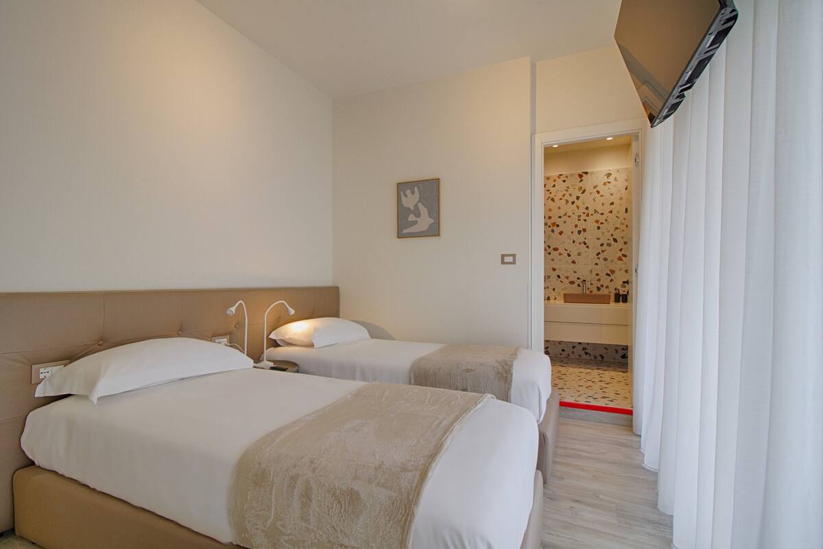 Habitación de hotel con dos camas, baño con ducha y televisor montado en la pared.
