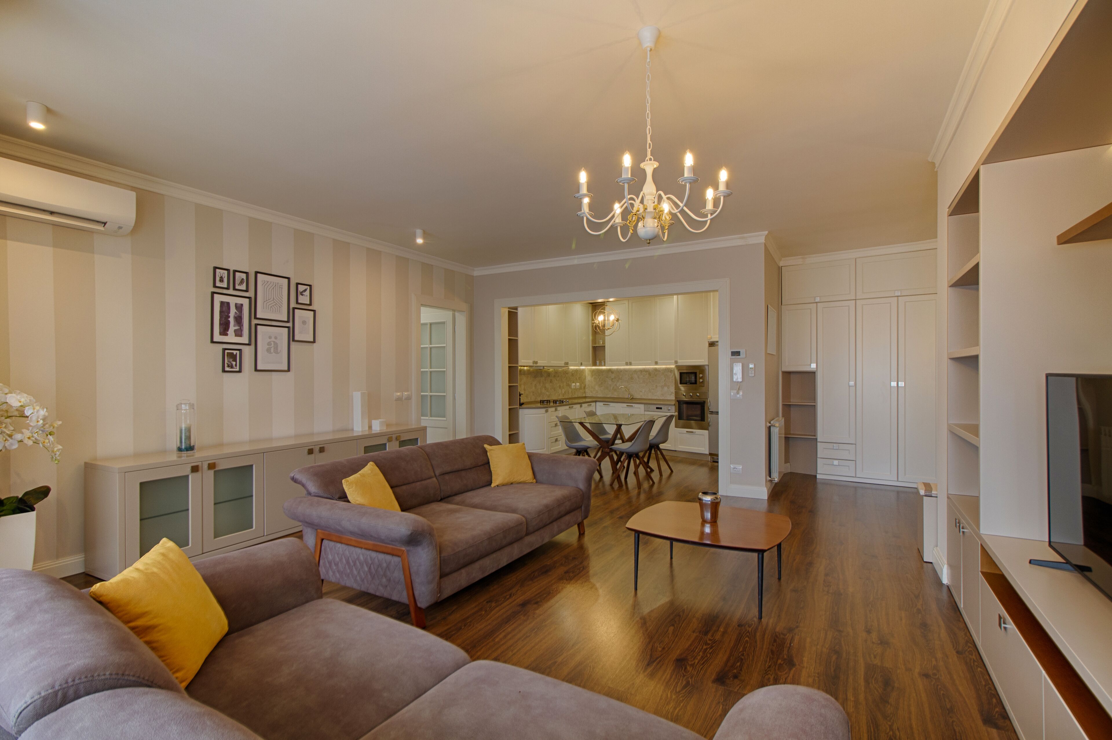 A modern living room with a sofa set, a dining table, and a kitchen area in the background.
