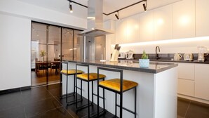 A modern kitchen with a central island, bar stools, and a dining area visible through glass doors.