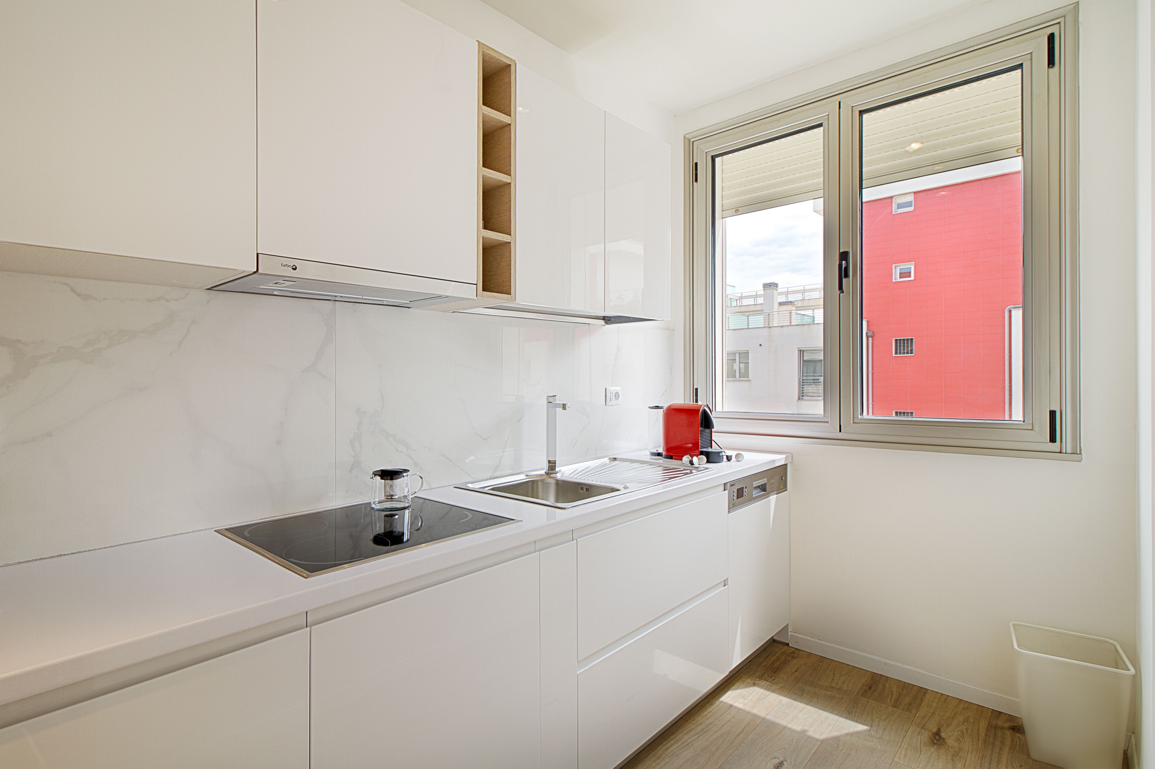 A modern kitchen with white cabinets, a built-in stove, and a window with a view of a red building.