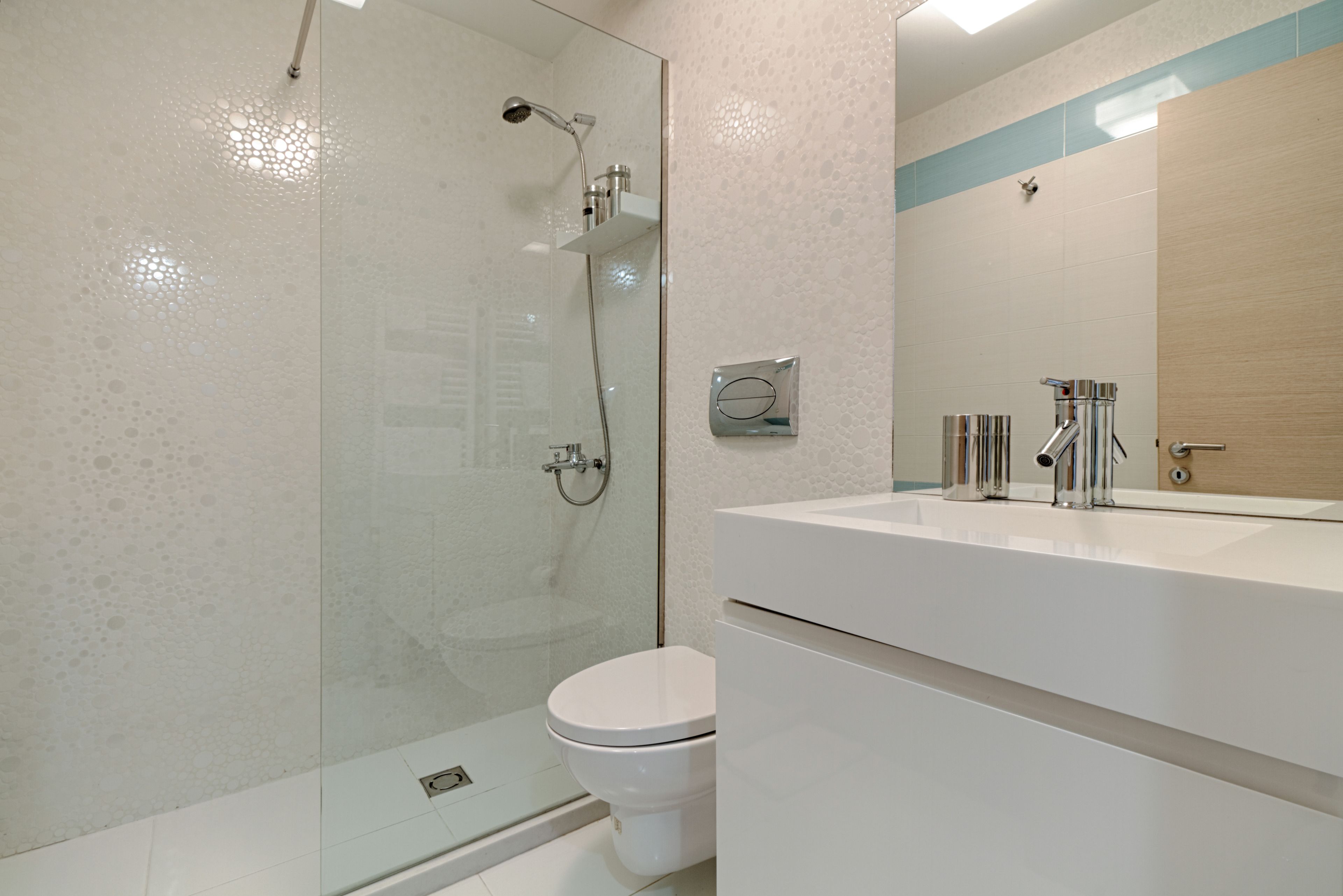 Un baño moderno con ducha de vidrio, inodoro blanco y un espejo grande sobre un lavabo blanco.