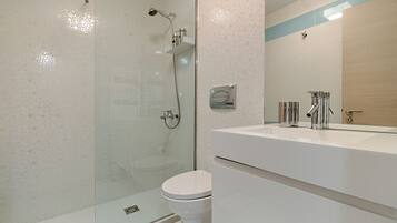 Un baño moderno con ducha de vidrio, inodoro blanco y un espejo grande sobre un lavabo blanco.