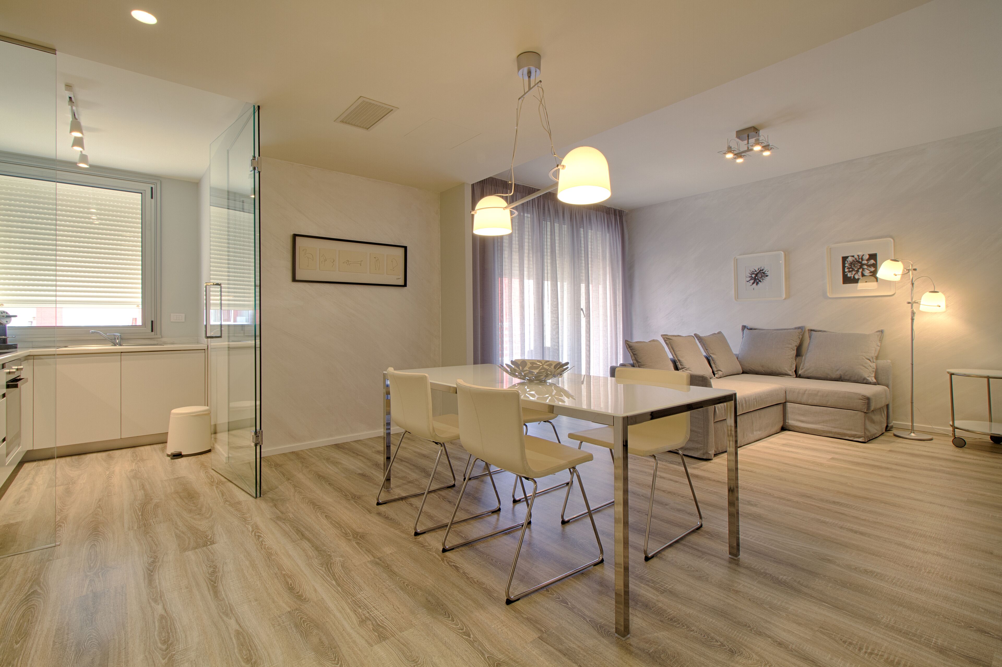 A modern living room with a glass partition, a dining table with chairs, a sofa, and a floor lamp.