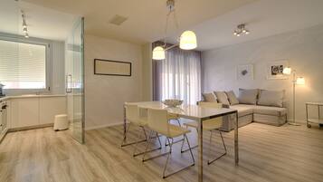 A modern living room with a glass partition, a dining table with chairs, a sofa, and a floor lamp.