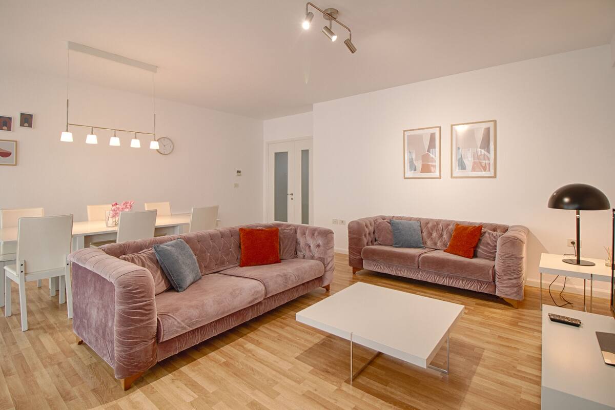 Una sala de estar moderna con dos sofás, una mesa de centro blanca y un comedor con sillas y una mesa.