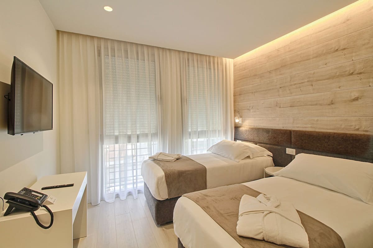 Una habitación de hotel con dos camas, un escritorio con teléfono y un televisor en la pared.