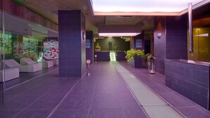 A modern lobby with a reception desk, seating area, and a hallway leading to the elevators.