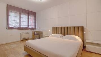 A bedroom with a large bed, a desk, a chair, and a window with blinds.