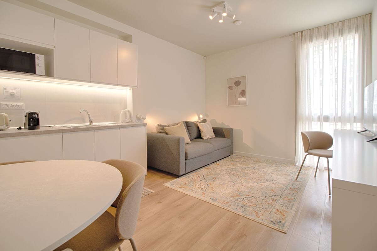 Un salón moderno y bien iluminado con cocina, una mesa de comedor y un sofá.