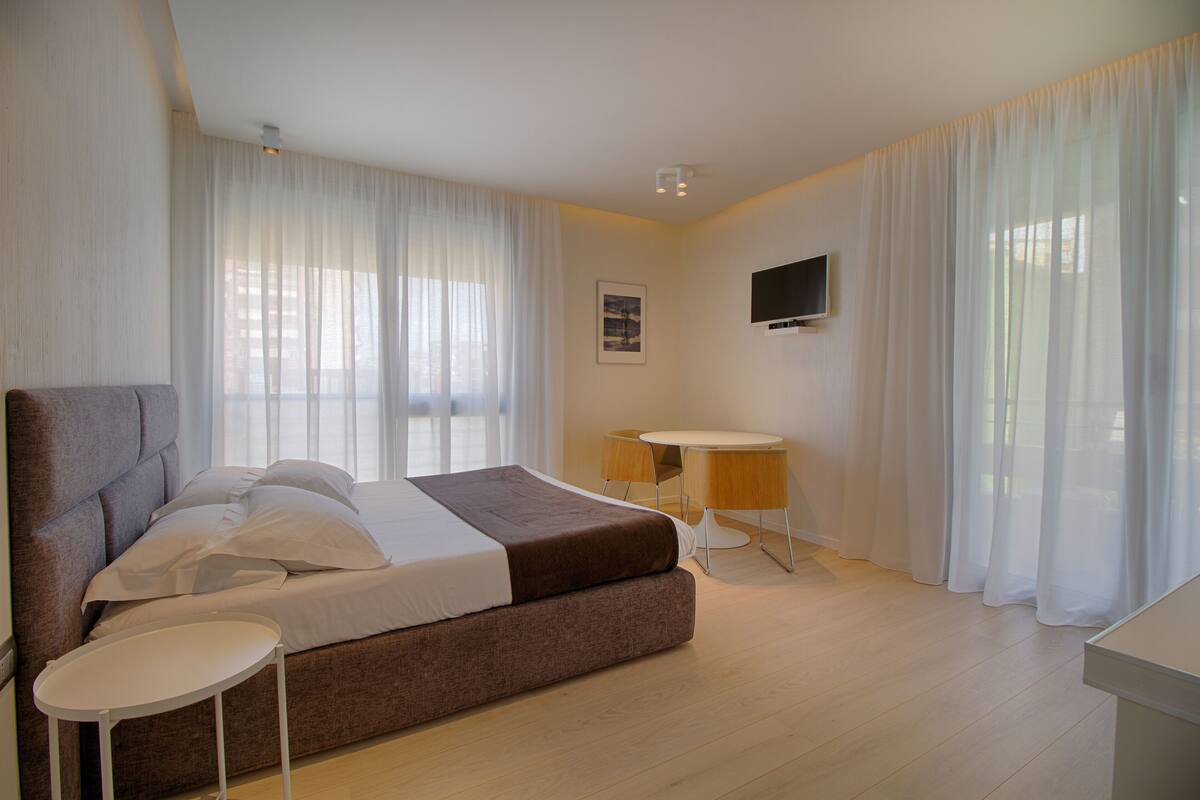 Un dormitorio moderno con una cama grande, una mesita redonda y un televisor en la pared.