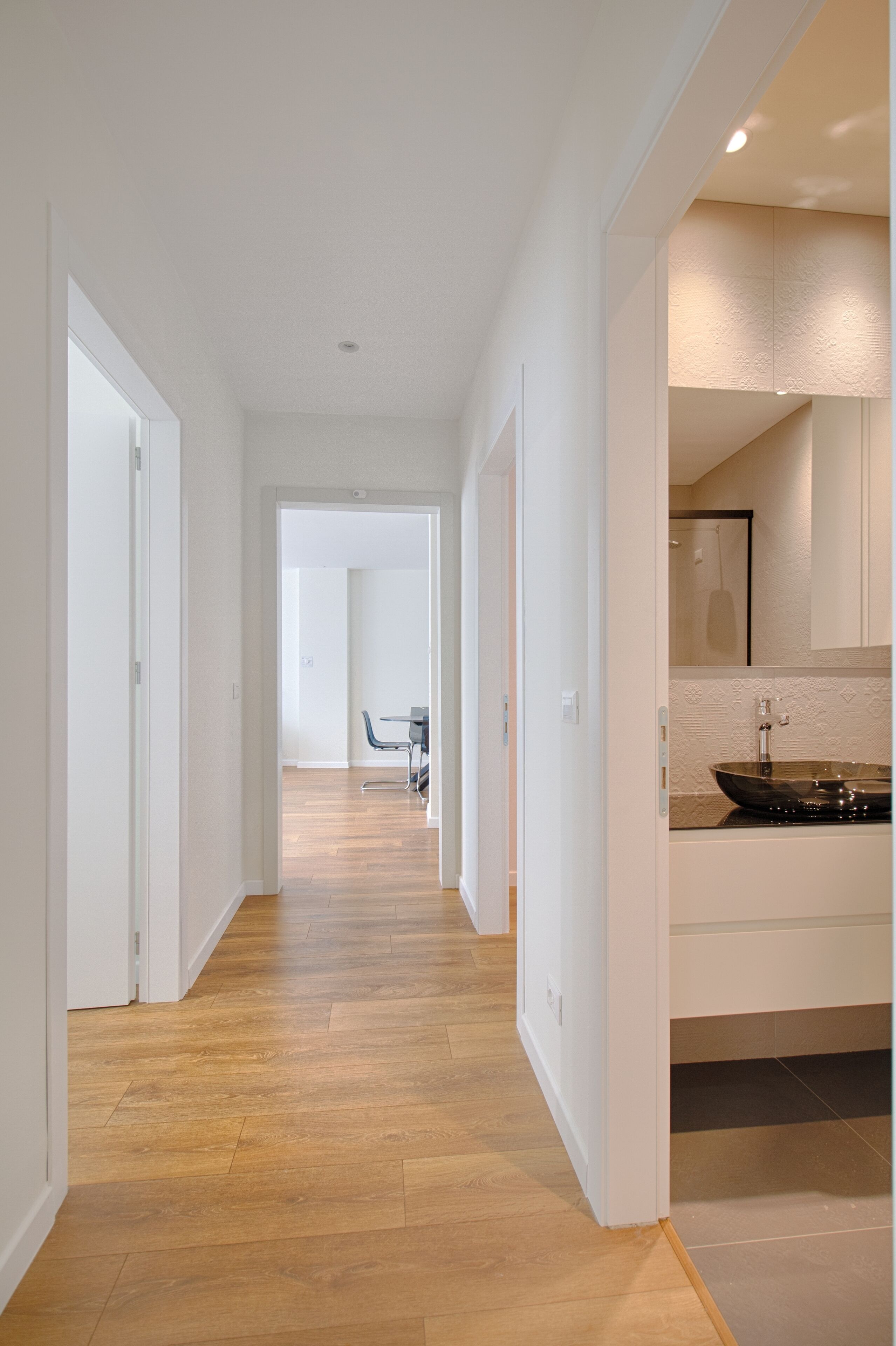 A modern kitchen with a large island, a dining area with a table and chairs, and a hallway with wooden flooring and white walls.