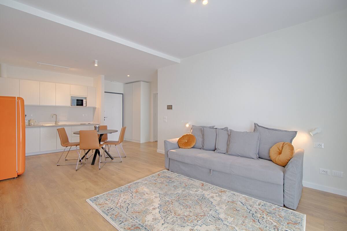 Una sala de estar moderna con un sofá gris, cojines anaranjados y una alfombra estampada.