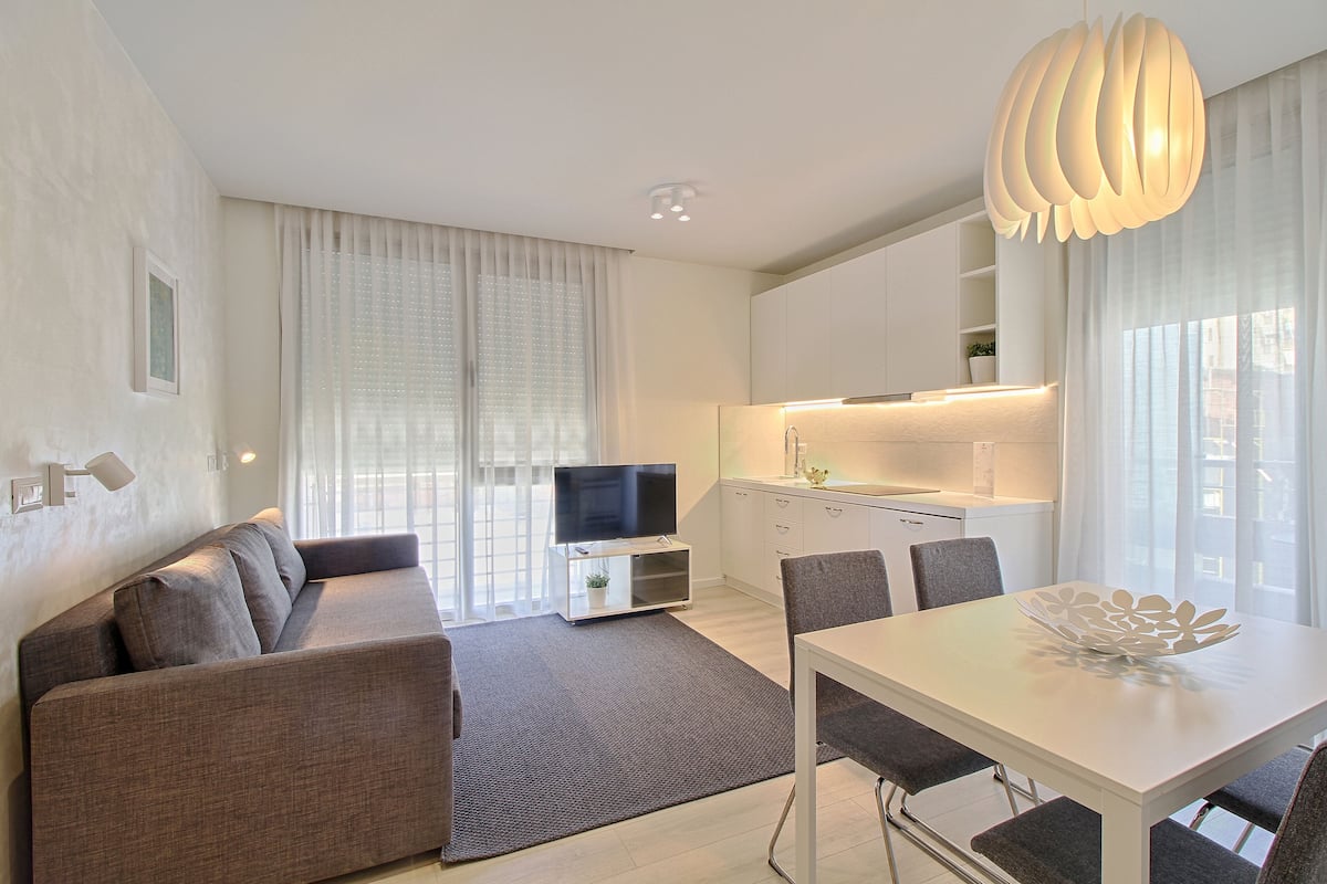 Una sala de estar moderna con sofá, televisor, mesa de comedor y sillas.