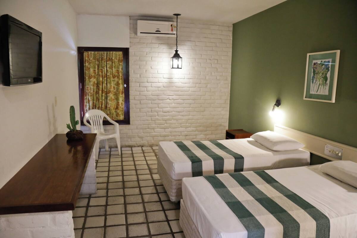 A room with two beds, a desk, a chair, a TV, and a painting on the wall.