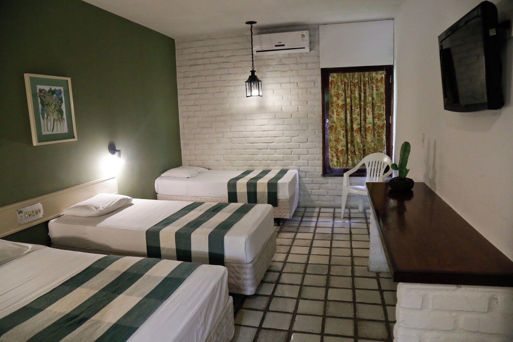 Una habitación con dos camas, una mesita, una silla, un aire acondicionado y un televisor en la pared.