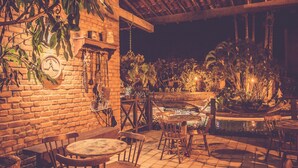 Un patio al aire libre con paredes de ladrillo, mesas y sillas de madera y una pequeña fuente de agua.