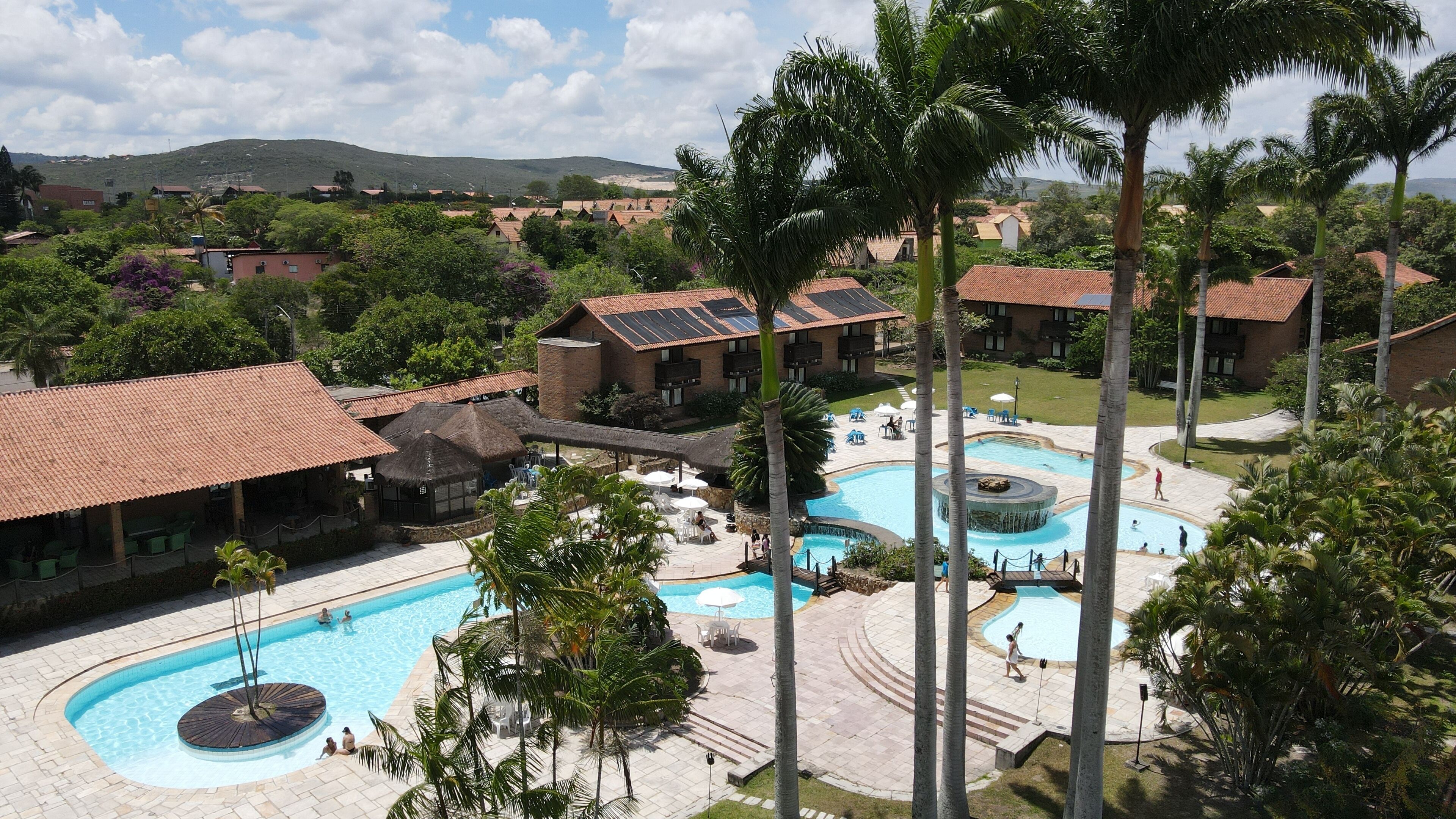 A resort with a central swimming pool, multiple smaller pools, and a landscaped area with palm trees.