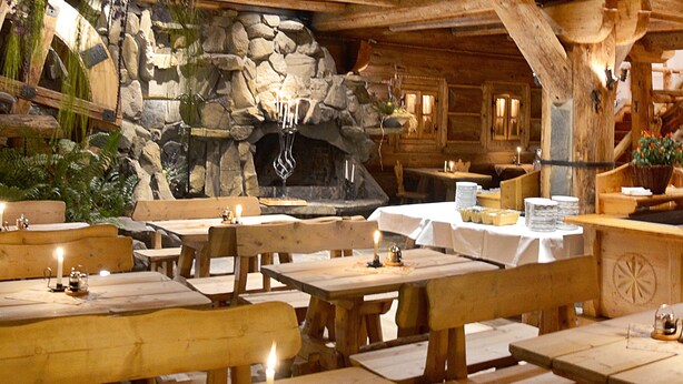 A rustic wooden interior with stone walls, wooden tables, benches, and hanging plants. - Hotel Sabala (Zakopane)