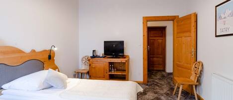 A bedroom with two beds, a wooden desk with a television, and a door leading to another room.