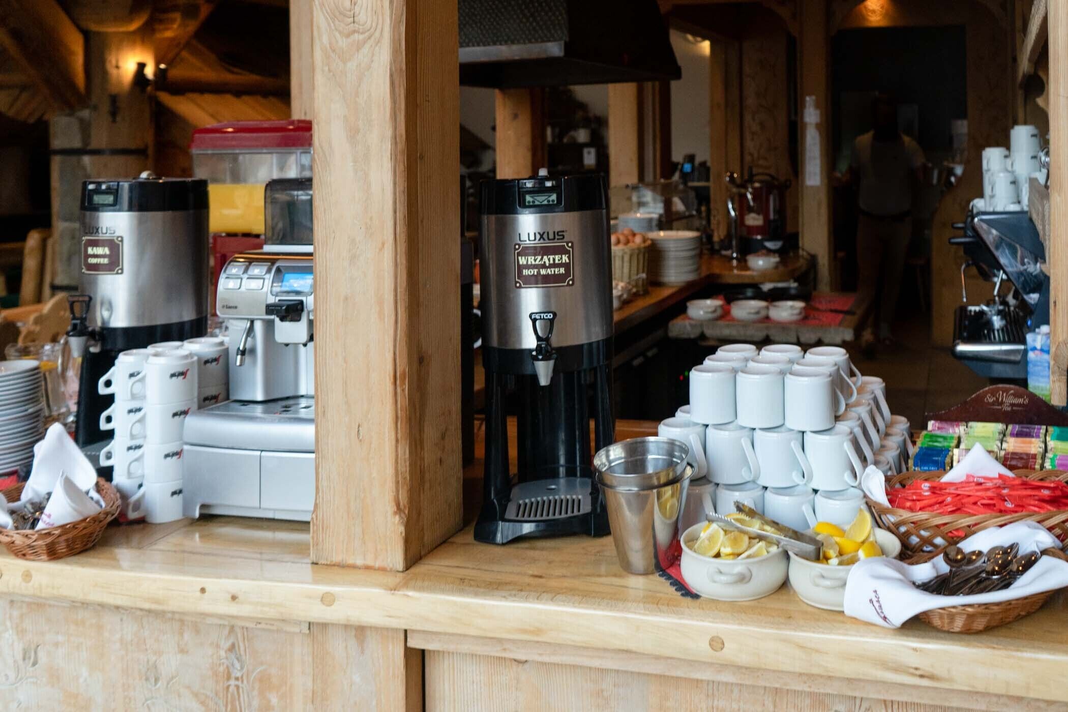 Una estación de café con varias máquinas, un dispensador de agua caliente y una variedad de tazas y utensilios.