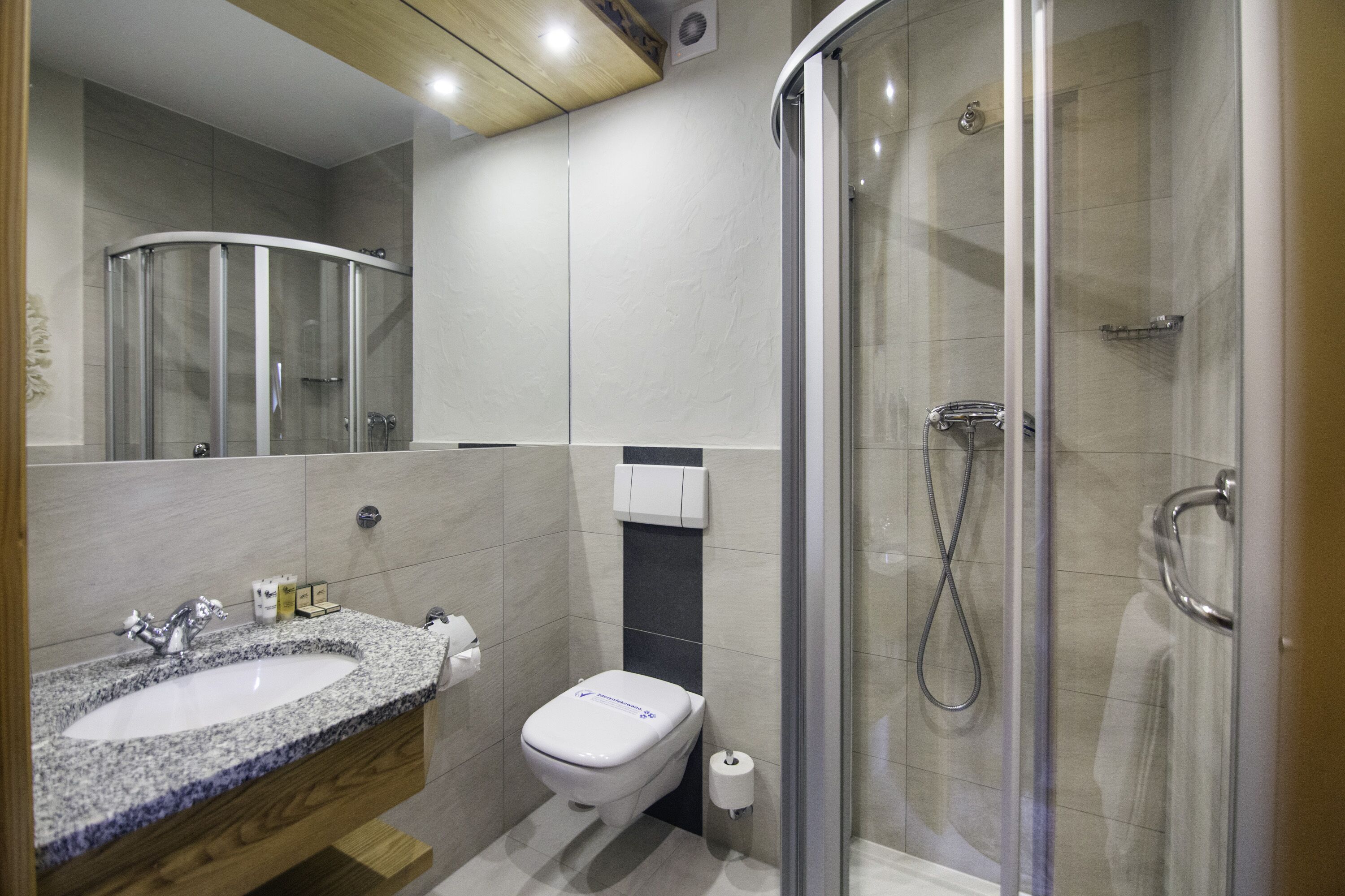 Un baño moderno con ducha envuelta en vidrio, lavamanos de granito y un inodoro.