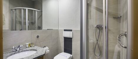 Un baño moderno con ducha envuelta en vidrio, lavamanos de granito y un inodoro.