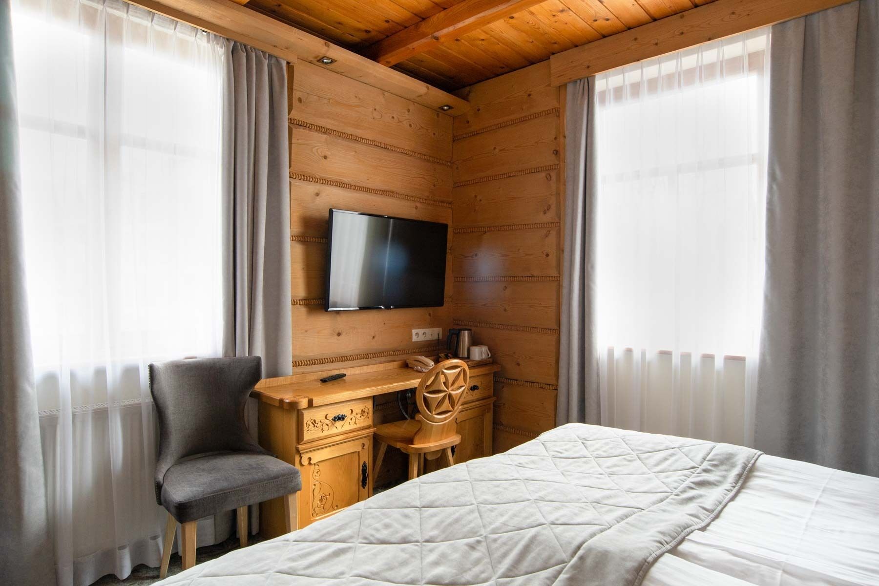 Una habitación de cabaña de madera con una cama, un escritorio, una silla, un televisor y cortinas.