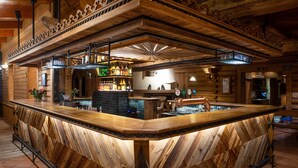 A bar area with a wooden bar counter, shelves with bottles, and a decorative ceiling. - Hotel Sabala (Zakopane)
