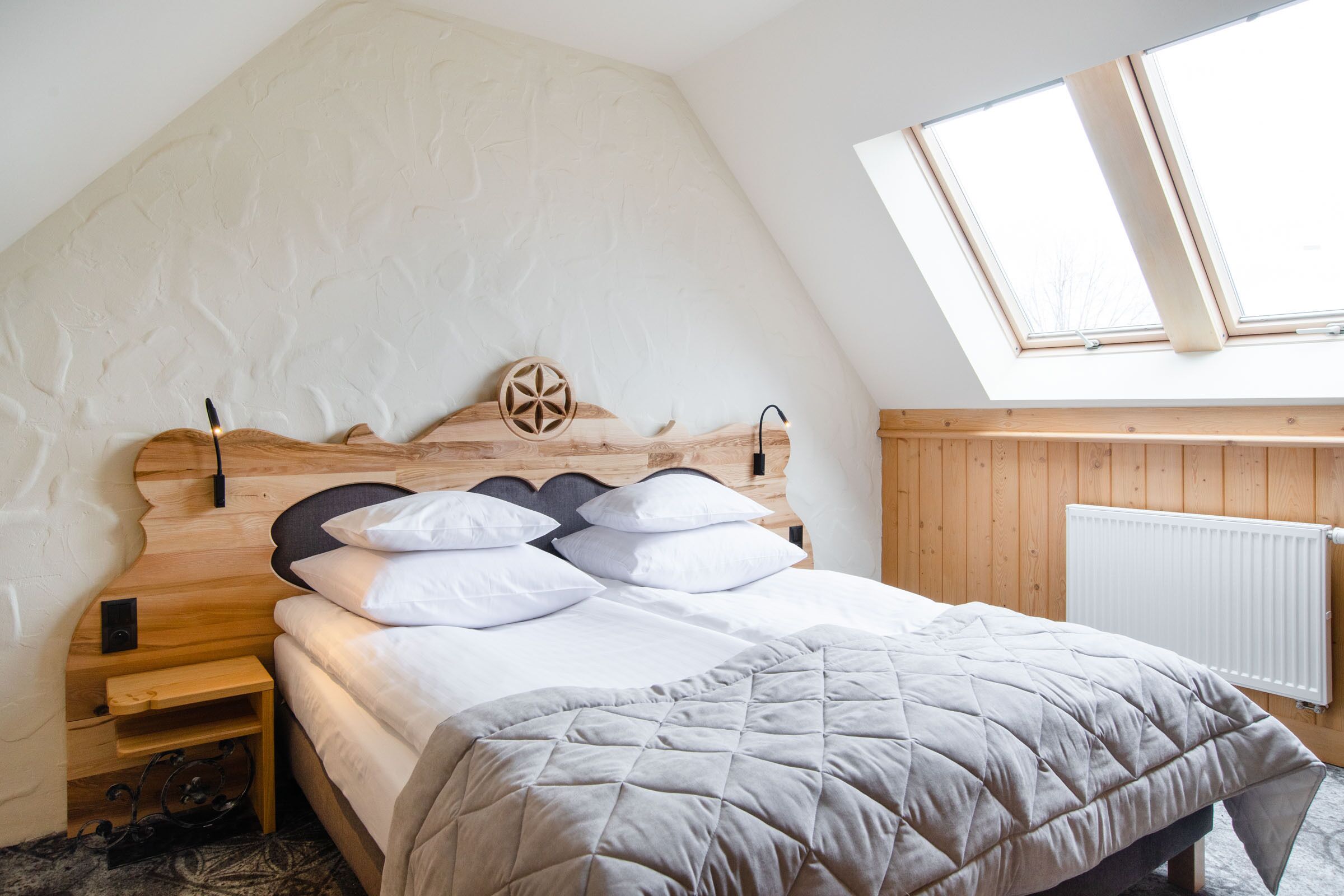 Une chambre avec un plafond en pente, une tête de lit en bois, un lit avec une literie blanche, une table de chevet et un puits de lumière.