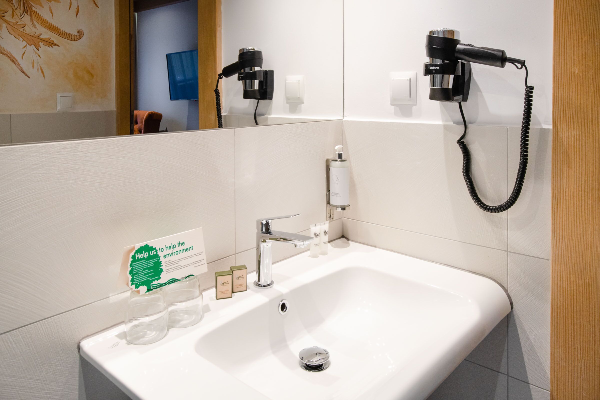 A bathroom with a white sink, two hair dryers mounted on the wall, and a mirror reflecting part of the room.