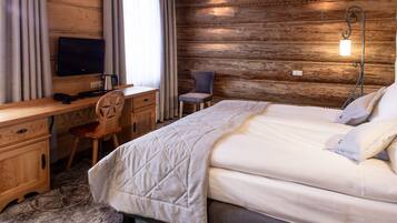 Habitación de hotel con pared de madera, cama con cubrecama acolchado, escritorio con ordenador y teléfono, y una silla.