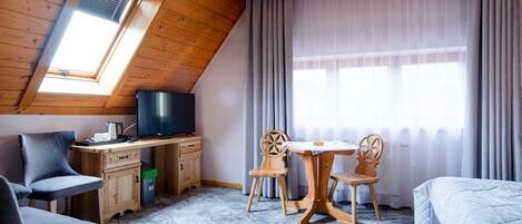 A cozy room with a sloped ceiling, wooden furniture, a television, a desk, a chair, a small table, and a bed.