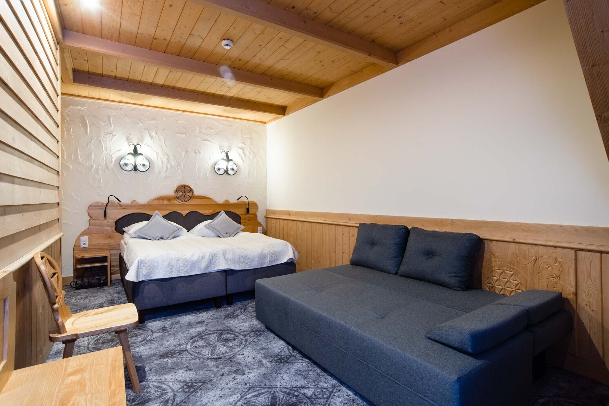 A cozy room with a bed, a sofa, a wooden chair, and a small table.