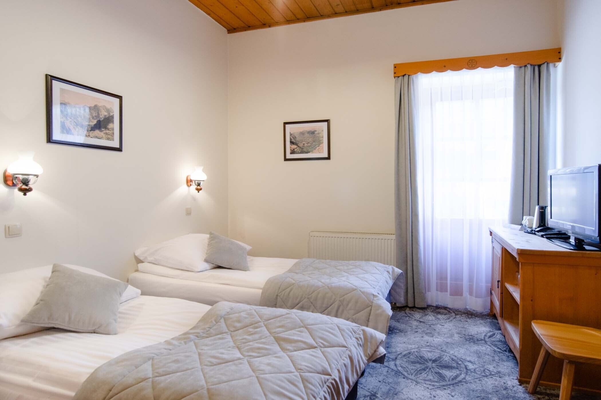 Ein Hotelzimmer mit zwei Betten, einem Schreibtisch mit Fernseher und zwei Wandleuchten.