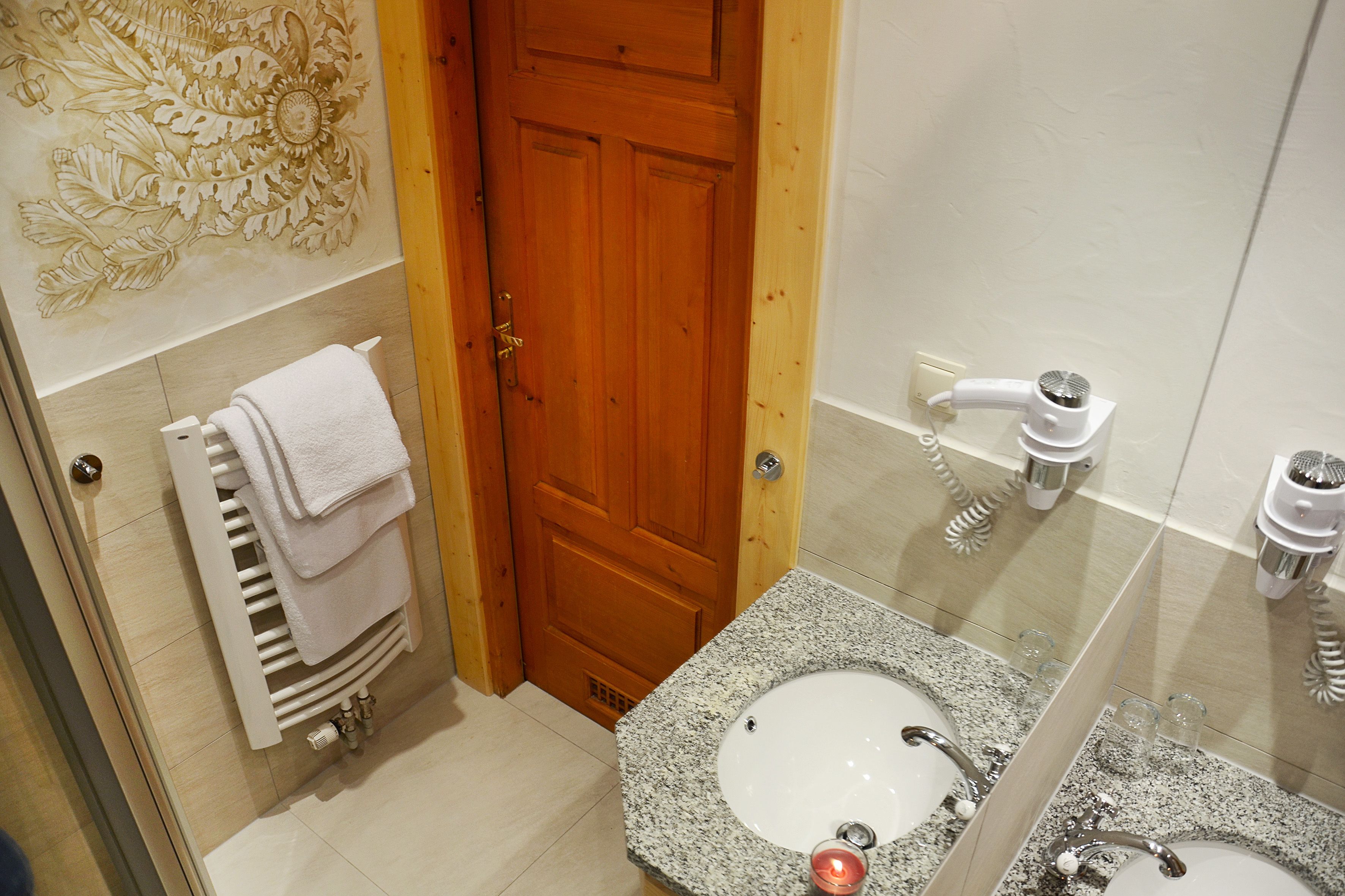 A bathroom with a wooden door, a towel rack with folded towels, a granite sink, and a hairdryer on the wall.